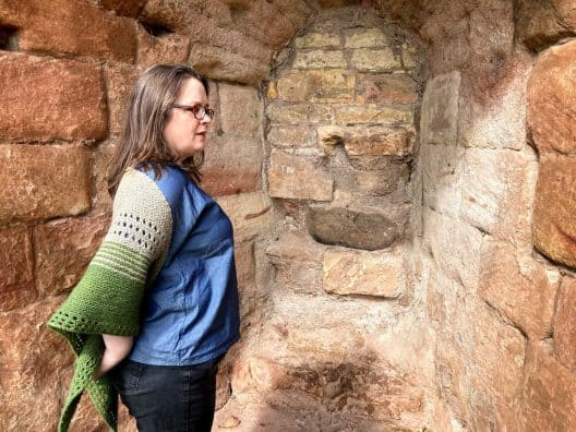 Louise stands in an alcove of pinkish stone. She stands with her right side toward the camera. She is wearing her gryer shawl around her shoulders.